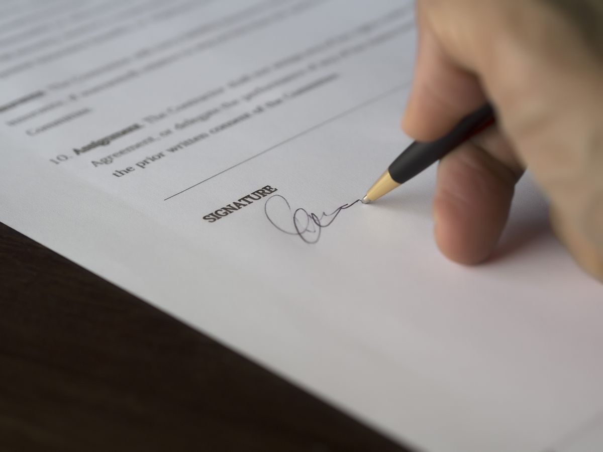 Hand signing a contract with a pen on a wooden desk
