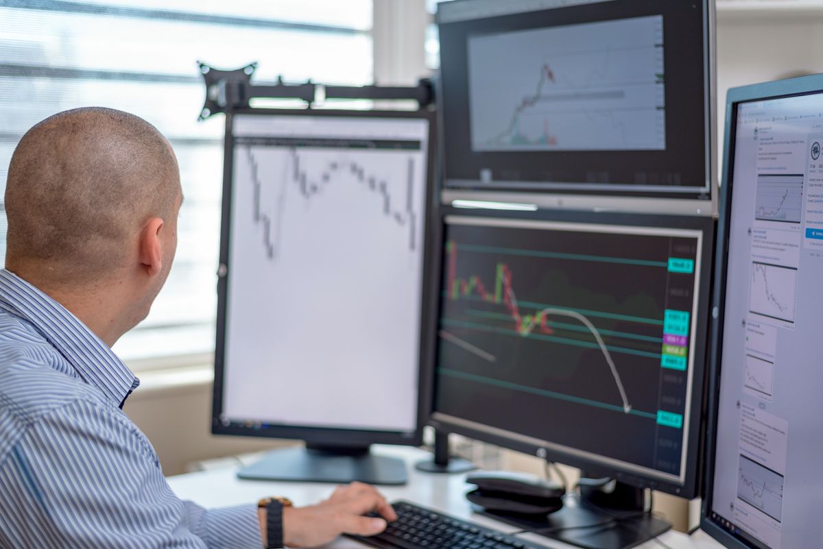 Person analyzing financial and marketing data across multiple monitors